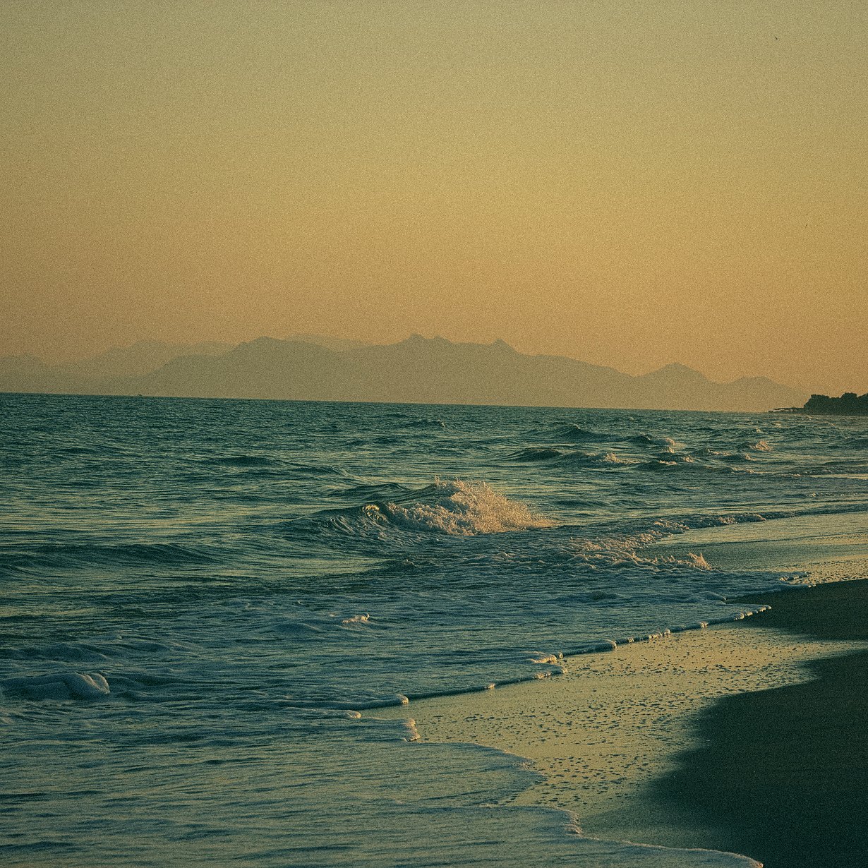 Waves at sunset with mountains on the horizon